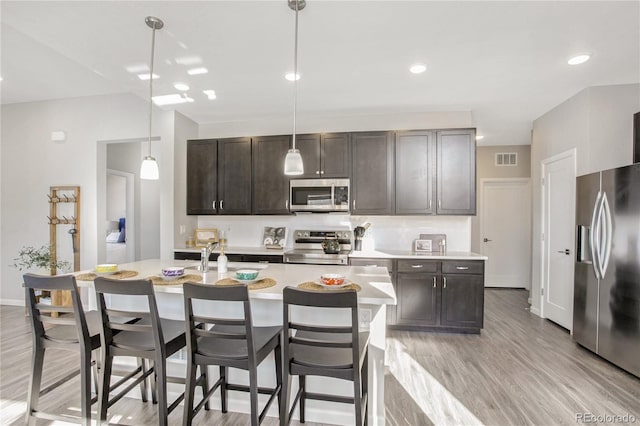 kitchen featuring pendant lighting, a kitchen island with sink, dark brown cabinetry, light hardwood / wood-style floors, and stainless steel appliances