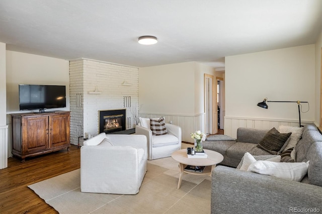 living area featuring a brick fireplace, wood finished floors, and wainscoting