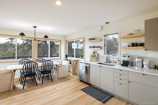 kitchen featuring hanging light fixtures, a sink, light countertops, open shelves, and stainless steel dishwasher