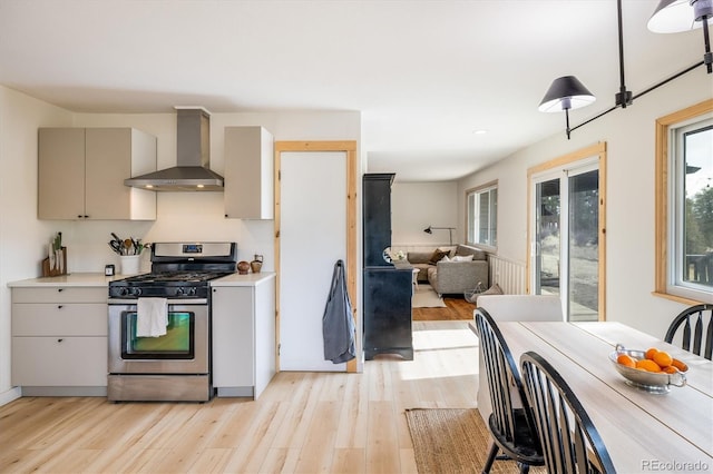 kitchen featuring light wood finished floors, light countertops, gas stove, open floor plan, and wall chimney range hood