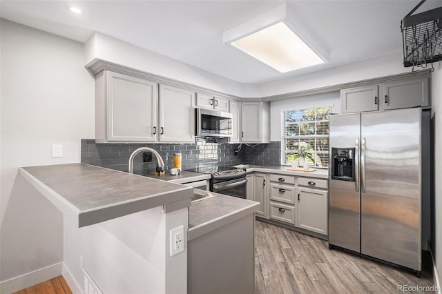 2882 W Long Cir Unit H, Littleton, CO 80120 - kitchen with appliances with stainless steel finishes, a peninsula, light wood-style flooring, tasteful backsplash, and gray cabinets