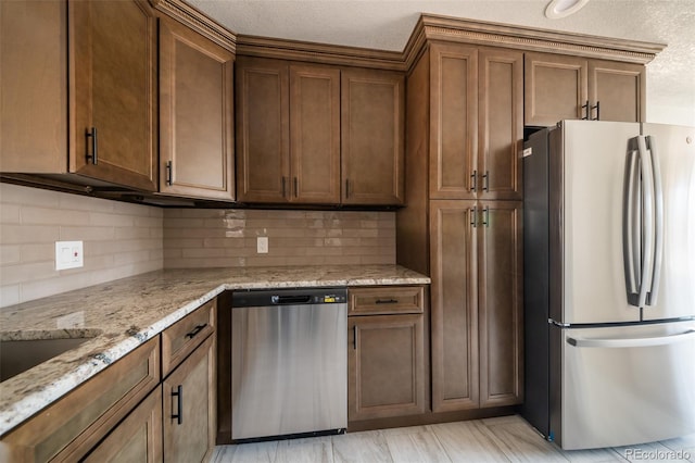 kitchen featuring appliances with stainless steel finishes, brown cabinets, light stone counters, a textured ceiling, and backsplash