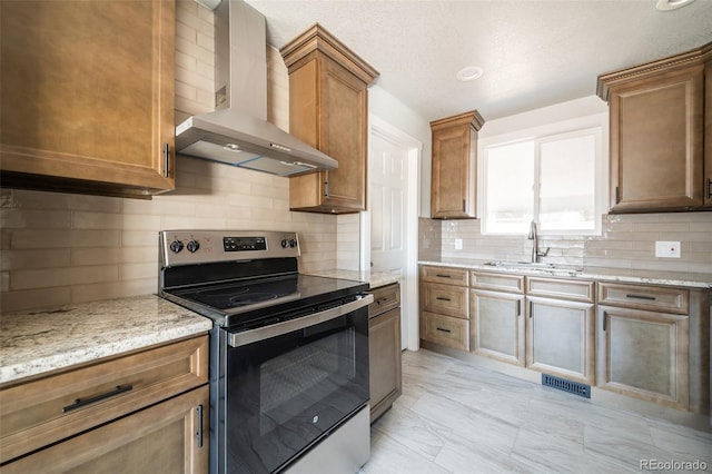 kitchen with visible vents, wall chimney exhaust hood, light stone counters, stainless steel electric stove, and a sink