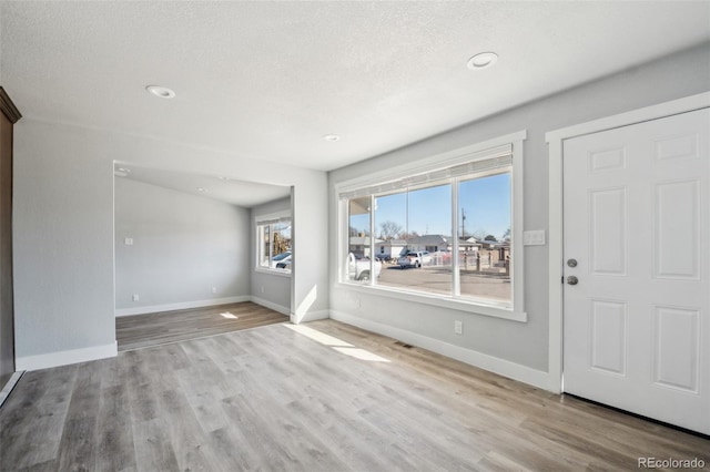 foyer entrance with a textured ceiling, baseboards, and wood finished floors