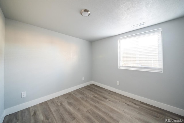 empty room with visible vents, a textured ceiling, baseboards, and wood finished floors