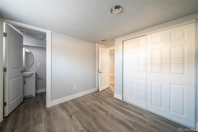 unfurnished bedroom featuring baseboards, visible vents, wood finished floors, a textured ceiling, and a closet