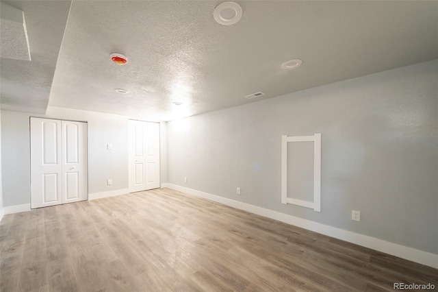 spare room with a textured ceiling, wood finished floors, visible vents, and baseboards