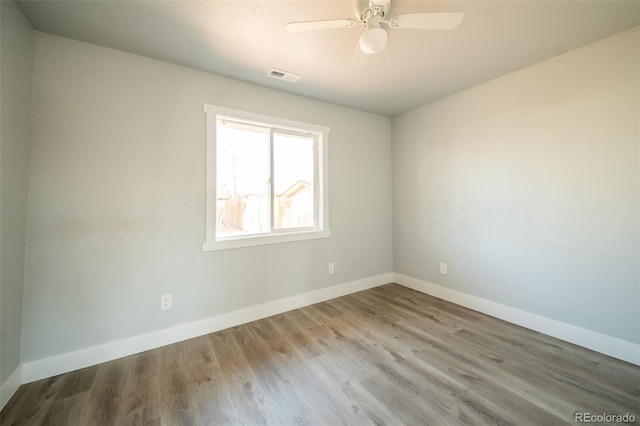 empty room featuring a ceiling fan, visible vents, baseboards, and wood finished floors