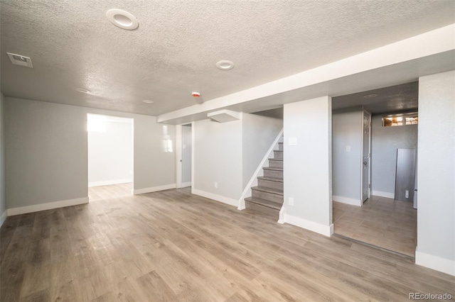 finished basement with visible vents, stairway, baseboards, and wood finished floors