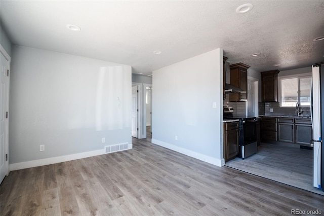 kitchen featuring range with electric cooktop, a sink, visible vents, wall chimney exhaust hood, and tasteful backsplash