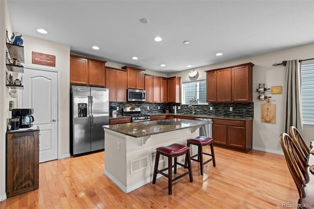 kitchen featuring dark stone counters, a kitchen breakfast bar, a kitchen island, stainless steel appliances, and light hardwood / wood-style floors