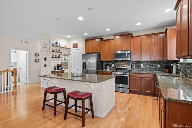 kitchen with sink, dark stone countertops, a kitchen island, stainless steel appliances, and a kitchen bar