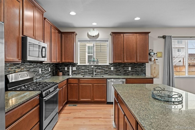 kitchen featuring sink, appliances with stainless steel finishes, dark stone countertops, tasteful backsplash, and light hardwood / wood-style floors