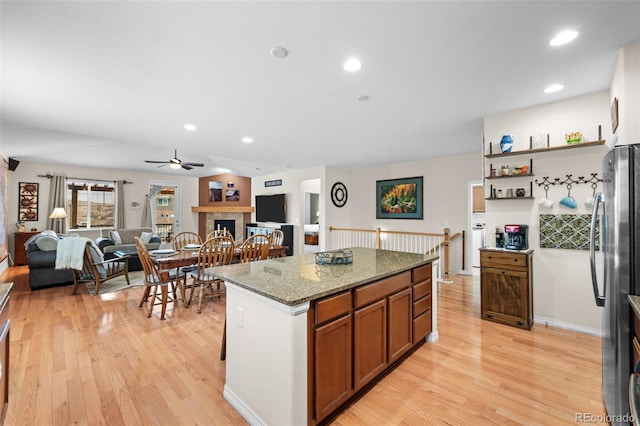 kitchen featuring light stone counters, light wood-type flooring, stainless steel fridge, a kitchen island, and a fireplace