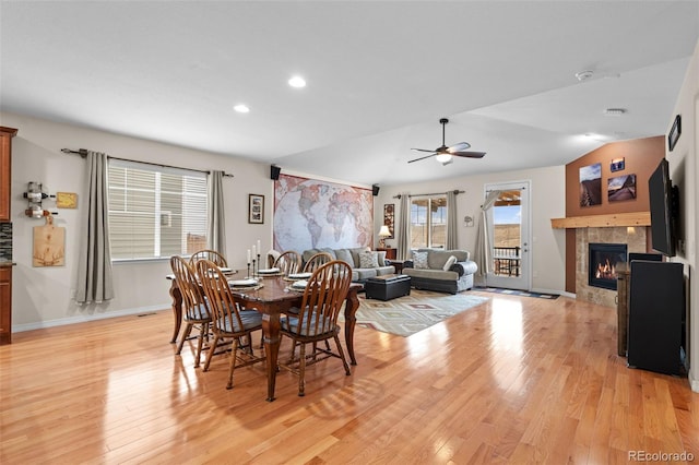 dining space featuring light hardwood / wood-style flooring, a tile fireplace, ceiling fan, and vaulted ceiling