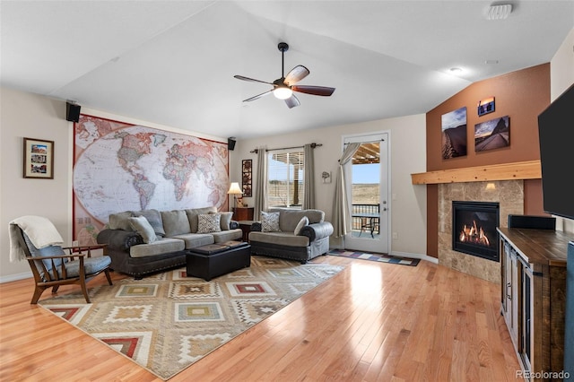 living room with lofted ceiling, light hardwood / wood-style flooring, a tile fireplace, and ceiling fan