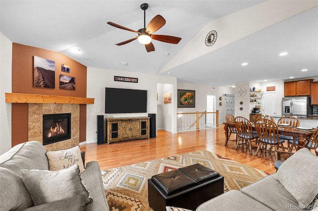 living room with light hardwood / wood-style flooring, a tile fireplace, ceiling fan, and vaulted ceiling