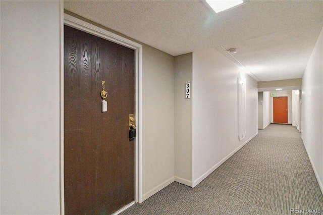 hall featuring baseboards, a textured ceiling, and carpet