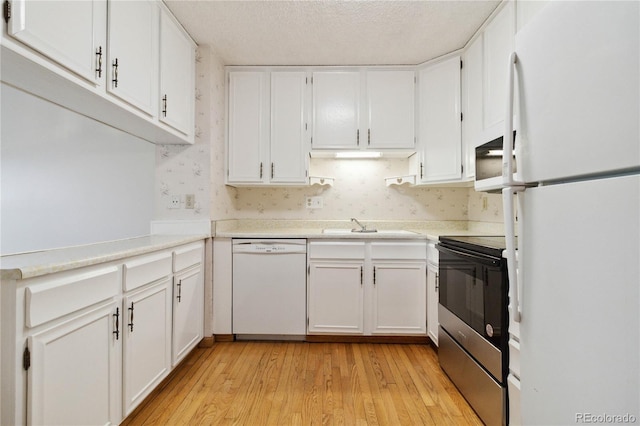 kitchen with light wood finished floors, white appliances, a textured ceiling, and white cabinetry