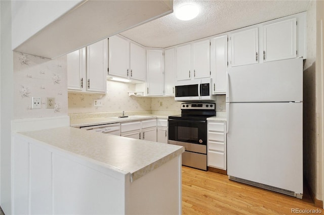 kitchen with white cabinets, a peninsula, light wood-style flooring, white appliances, and light countertops