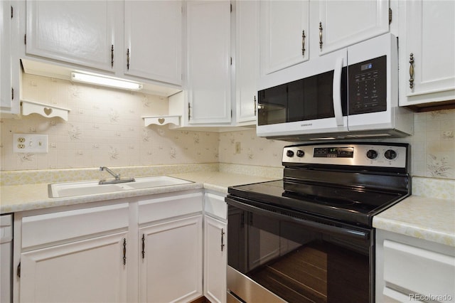 kitchen featuring a sink, electric range, white microwave, white cabinetry, and decorative backsplash