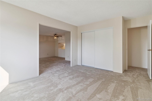 unfurnished bedroom featuring a textured ceiling, a closet, and light colored carpet