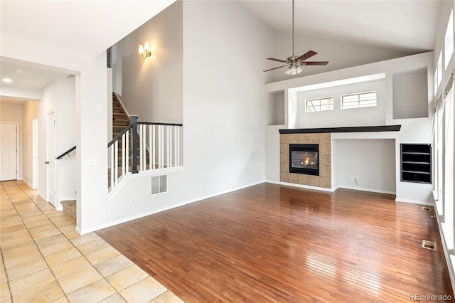 4488 Larksong Pl, Castle Rock, CO 80109 - unfurnished living room with hardwood / wood-style flooring, stairway, ceiling fan, a tiled fireplace, and high vaulted ceiling
