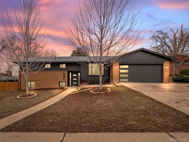 mid-century modern home featuring brick siding, concrete driveway, an attached garage, and fence