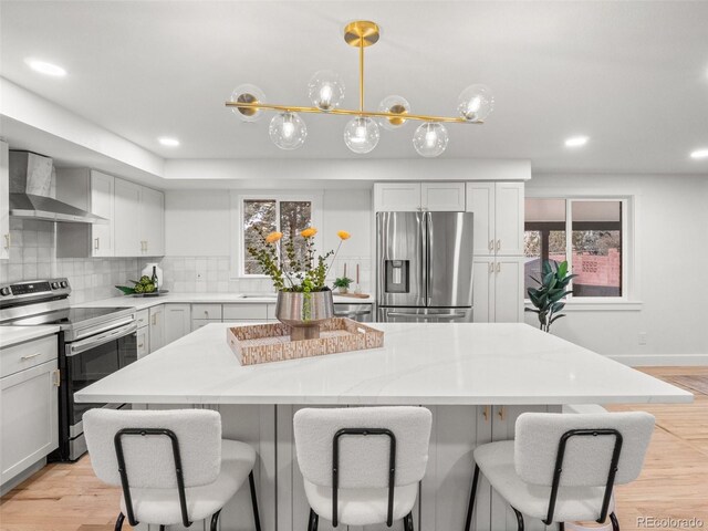 kitchen featuring a kitchen island, a breakfast bar, stainless steel appliances, wall chimney range hood, and backsplash