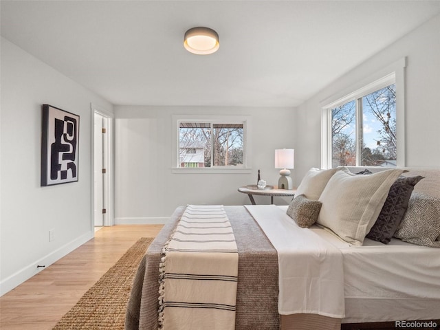 bedroom featuring multiple windows, baseboards, and light wood-style floors