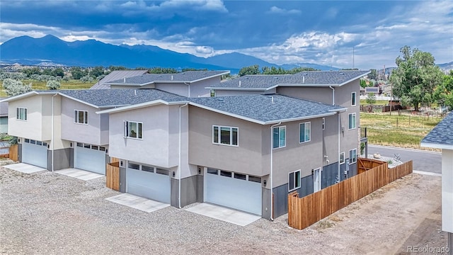 exterior space with roof with shingles, an attached garage, fence, a mountain view, and driveway