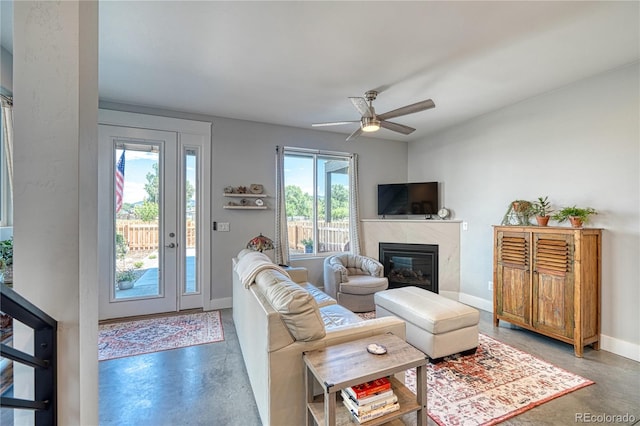 living room featuring finished concrete floors, baseboards, a fireplace, and a ceiling fan