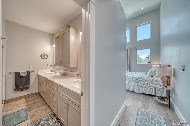 ensuite bathroom featuring double vanity, a sink, ensuite bath, and wood finished floors