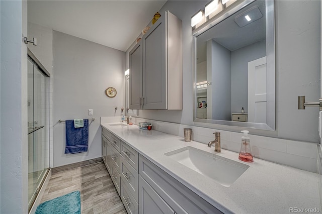 full bathroom featuring double vanity, wood finished floors, a stall shower, and a sink