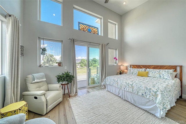 bedroom featuring access to exterior, a high ceiling, and wood finished floors