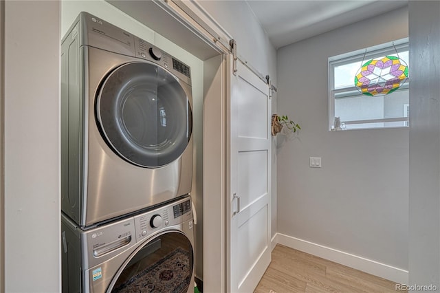 clothes washing area featuring laundry area, a barn door, baseboards, stacked washer / drying machine, and light wood-type flooring