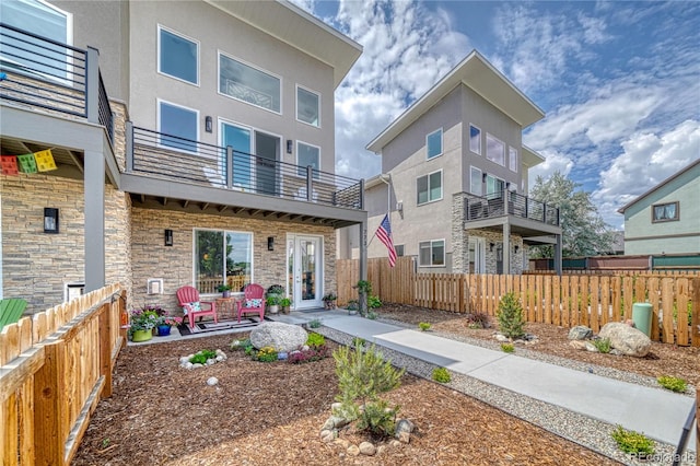 back of property featuring stone siding, fence, a balcony, and stucco siding