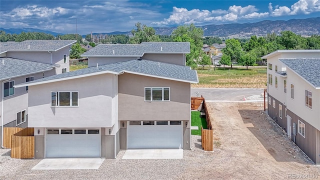 view of front facade with driveway, roof with shingles, a mountain view, and stucco siding