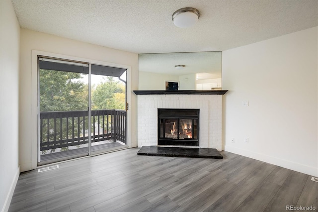 unfurnished living room featuring hardwood / wood-style floors, a textured ceiling, and a brick fireplace