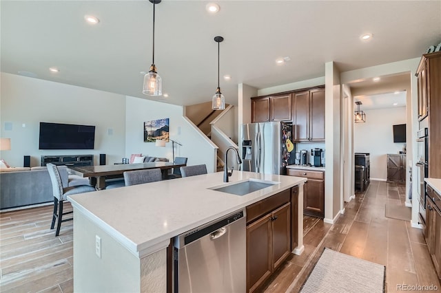 kitchen featuring light wood-style flooring, an island with sink, a sink, appliances with stainless steel finishes, and open floor plan