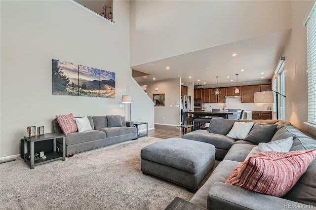 living area with light carpet, recessed lighting, a high ceiling, and baseboards