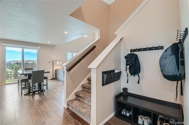 stairway featuring recessed lighting, a textured ceiling, baseboards, and wood finished floors