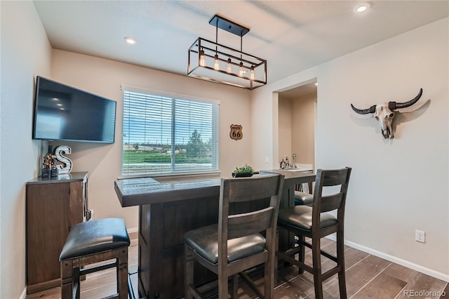 dining room with recessed lighting, a bar, dark wood-type flooring, and baseboards