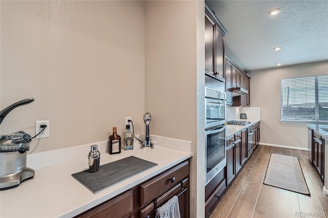 kitchen with stainless steel gas cooktop, dark brown cabinets, wood tiled floor, and light countertops