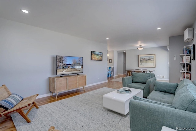 living room featuring a wall unit AC, baseboards, wood finished floors, and recessed lighting