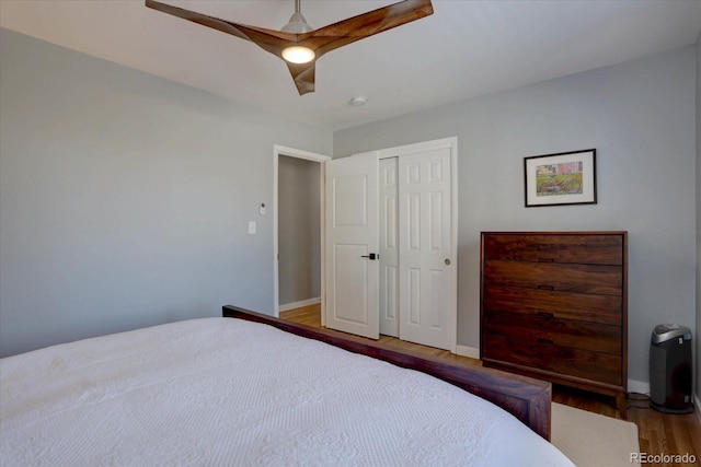 bedroom featuring a closet, wood finished floors, a ceiling fan, and baseboards