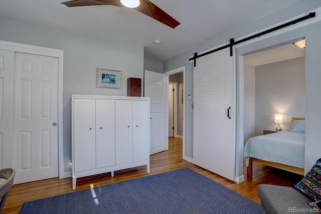 bedroom with baseboards, a ceiling fan, a barn door, and wood finished floors