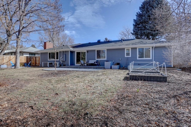 rear view of house with a patio area, a lawn, a chimney, and fence