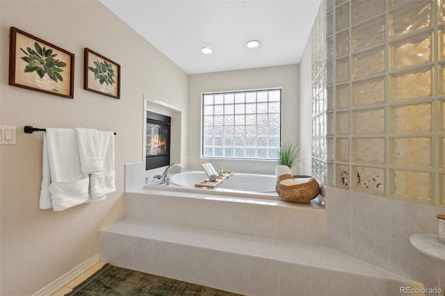 full bathroom with a garden tub and a glass covered fireplace