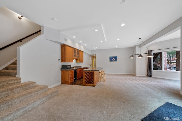 kitchen with a breakfast bar area, light carpet, open floor plan, brown cabinetry, and dark countertops